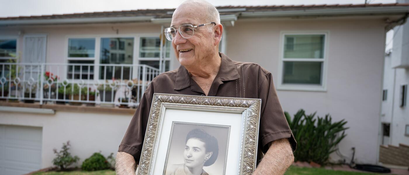 An elderly man, holding a black-and-white photo of his mother, stands in front of his Little Italy home. 
