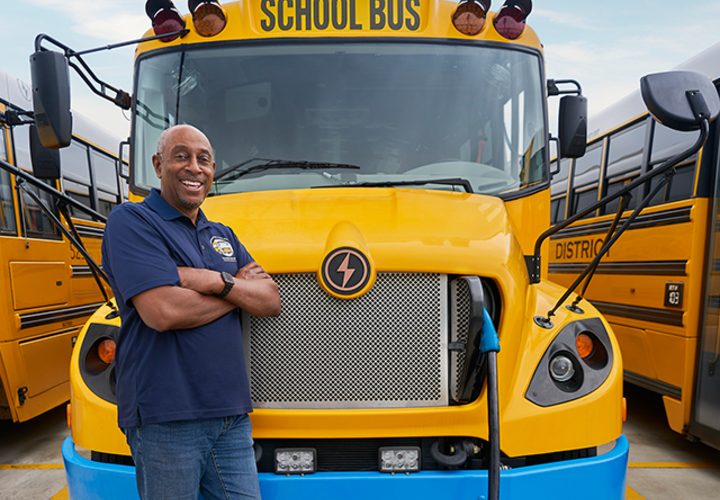 Cajon Valley Bus Driver smiling as he leans against his parked electric bus