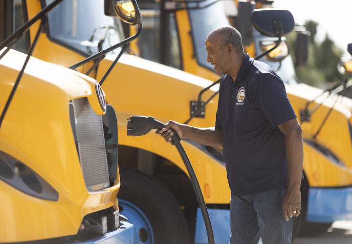 School bus driver plugging in an electric yellow school bus to charge