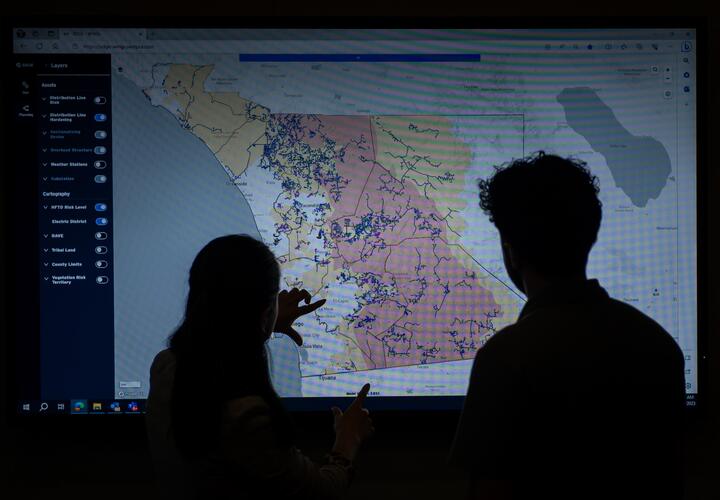 Member's of SDG&E Meteorology team point at a screen, showing a map with data related to the company's service territory.