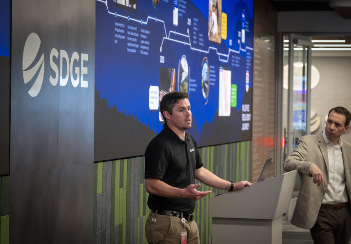 SDGE Communications Manager, Alex Welling, delivers opening remarks in front of a large screen at the media event. 
