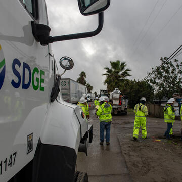 An SDG&E vehicle with field workers wearing bright yellow vests in the background.