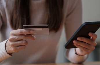 A photo of a woman holding her mobile phone in one hand, and a credit card in the other. 