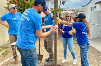 Employee volunteers wearing blue shirts plant a small tree. 