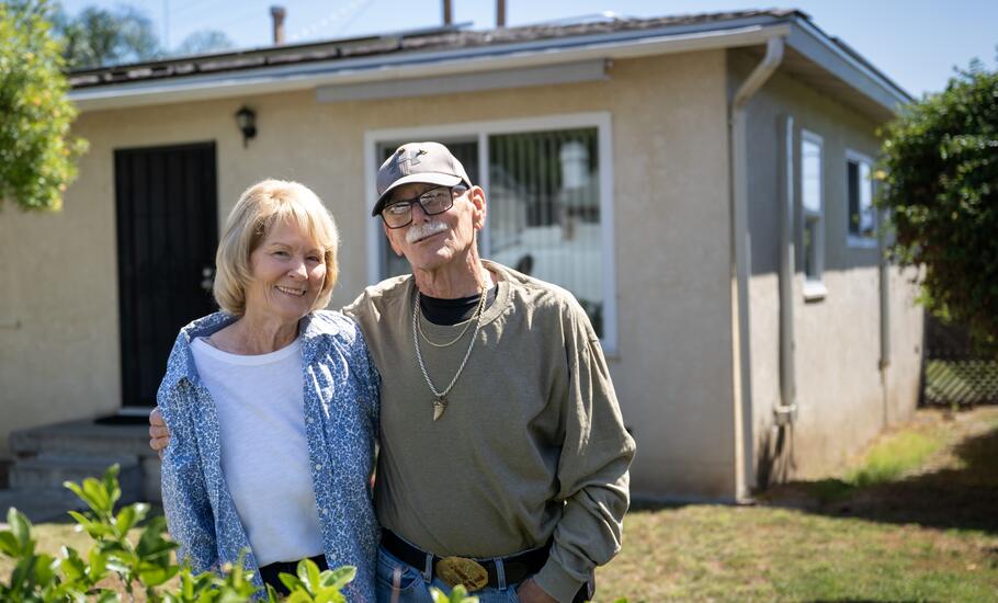 A man and women pose for a photo outside their home.
