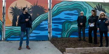Local artist Stiles-Mikl with the vibrant mural he created behind him.
