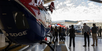 An image that shows the back of a helicopter with an SDG&E logo and a press conference taking place in the background.