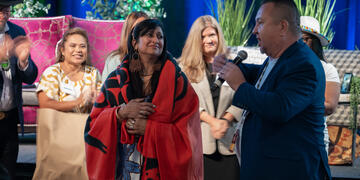 A man holding a mic at the Tribal summit, interacting with a woman wearing a red shawl.